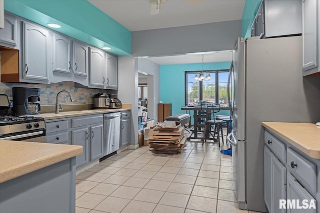 kitchen featuring stainless steel appliances, gray cabinets, light tile patterned floors, a sink, and a chandelier