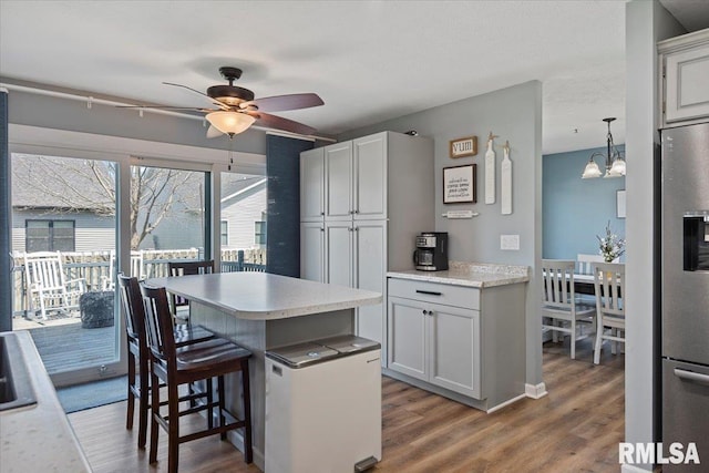 kitchen with light countertops, a kitchen island, a kitchen bar, stainless steel fridge, and ceiling fan with notable chandelier
