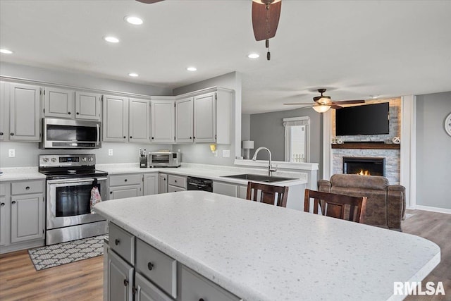 kitchen featuring a sink, light wood-type flooring, a fireplace, appliances with stainless steel finishes, and ceiling fan