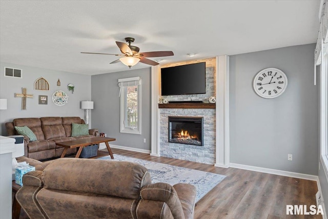 living room with ceiling fan, baseboards, a stone fireplace, and visible vents
