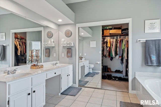 bathroom with tile patterned floors, double vanity, toilet, a sink, and a walk in closet