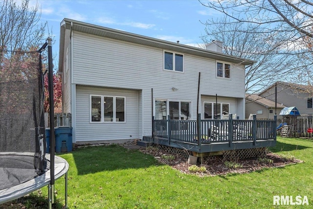 rear view of property featuring a wooden deck, a chimney, a yard, and a trampoline