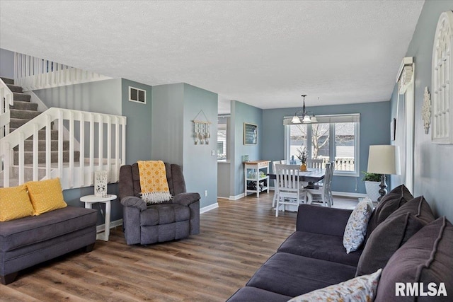 living area with an inviting chandelier, wood finished floors, visible vents, baseboards, and stairs