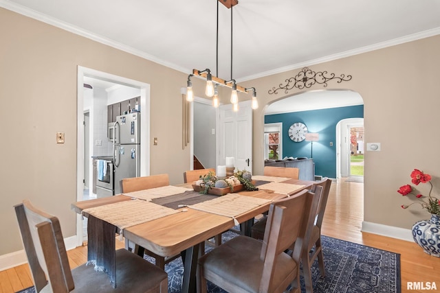dining room with arched walkways, ornamental molding, wood finished floors, and baseboards