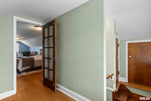 corridor featuring hardwood / wood-style flooring, vaulted ceiling, and baseboards