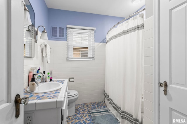 full bathroom featuring visible vents, toilet, vanity, tile walls, and wainscoting