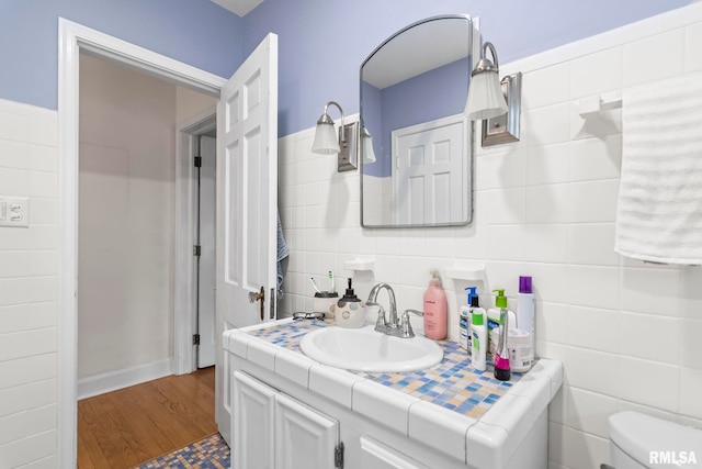 bathroom with tile walls, toilet, vanity, and wood finished floors