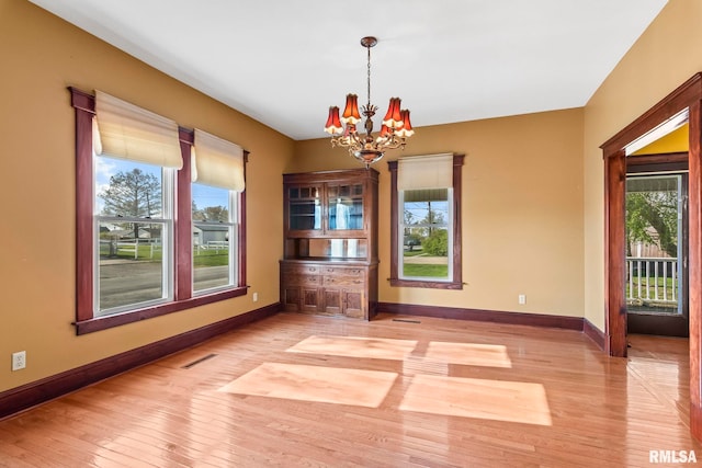 101 E Lester St, Williamsville, IL 62693 - empty room featuring light wood-style flooring, a healthy amount of sunlight, baseboards, and an inviting chandelier