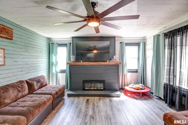 living room featuring plenty of natural light, wood finished floors, wood walls, and a glass covered fireplace