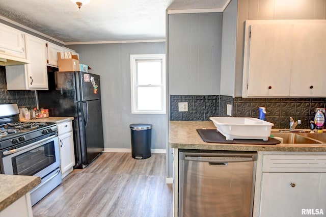 kitchen with crown molding, a sink, light wood-type flooring, backsplash, and appliances with stainless steel finishes