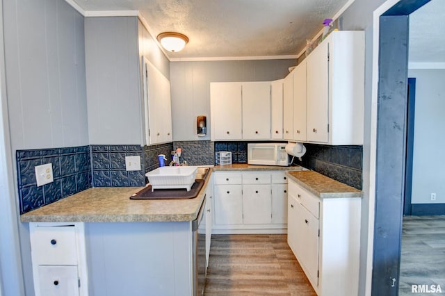 kitchen featuring backsplash, crown molding, light wood-style floors, and white microwave