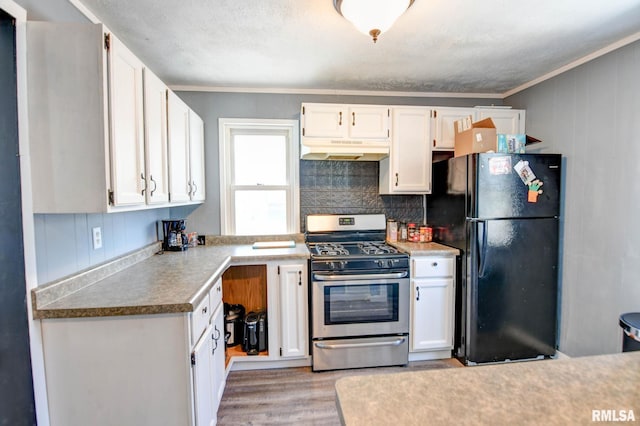 kitchen featuring white cabinets, freestanding refrigerator, gas range, and under cabinet range hood