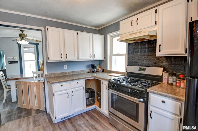 kitchen with freestanding refrigerator, wood finished floors, stainless steel gas range, and under cabinet range hood
