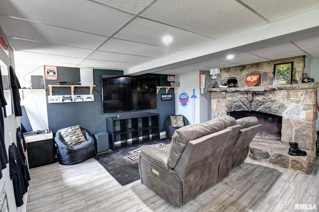living area featuring a paneled ceiling, a stone fireplace, and wood finished floors