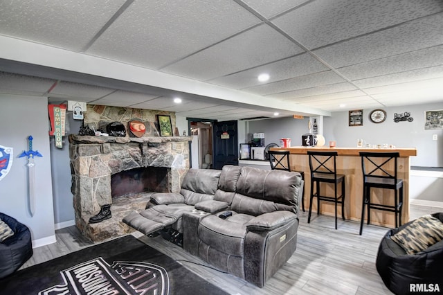 living area featuring a paneled ceiling, a bar, baseboards, and light wood-type flooring