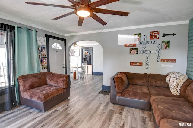 living room featuring arched walkways, a ceiling fan, light wood finished floors, and a healthy amount of sunlight