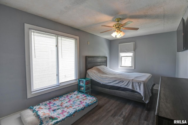 bedroom with a textured ceiling, a ceiling fan, dark wood-style floors, and multiple windows