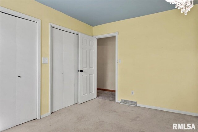 unfurnished bedroom with carpet floors, a notable chandelier, visible vents, baseboards, and multiple closets