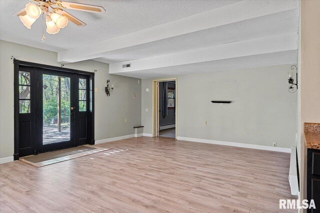 unfurnished living room featuring light wood-style floors, visible vents, baseboards, a textured ceiling, and baseboard heating