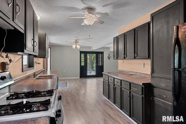 kitchen with gas range, light wood-style floors, a sink, a ceiling fan, and a textured ceiling