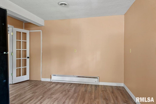empty room with wood finished floors, a baseboard heating unit, baseboards, visible vents, and a textured ceiling