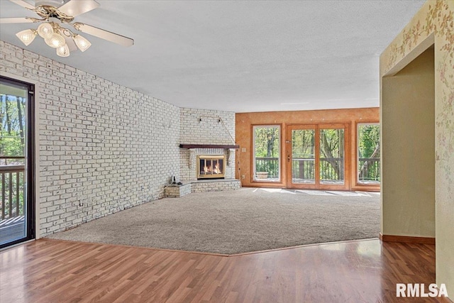 unfurnished living room featuring a wealth of natural light, wood finished floors, baseboards, and a brick fireplace