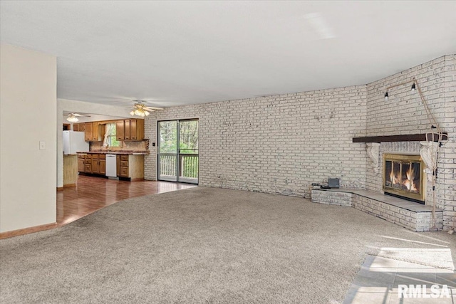 unfurnished living room featuring dark colored carpet, ceiling fan, baseboards, brick wall, and a fireplace