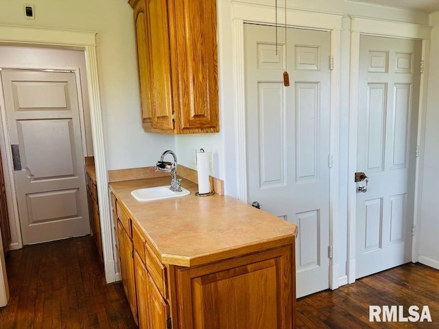 kitchen with light countertops, dark wood finished floors, brown cabinetry, and a sink