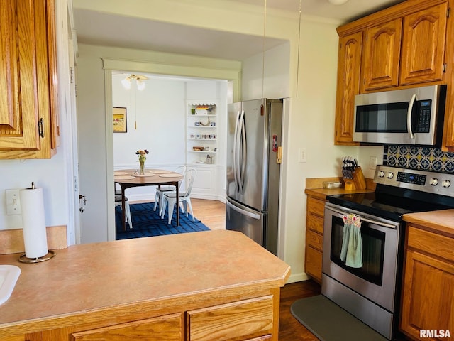 kitchen with stainless steel appliances, dark wood finished floors, tasteful backsplash, brown cabinets, and light countertops