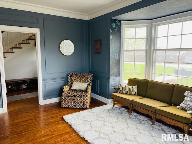 living area featuring a decorative wall, ornamental molding, wood finished floors, and stairs