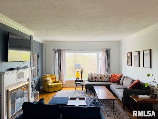 living area with a glass covered fireplace, wood finished floors, a textured ceiling, and crown molding