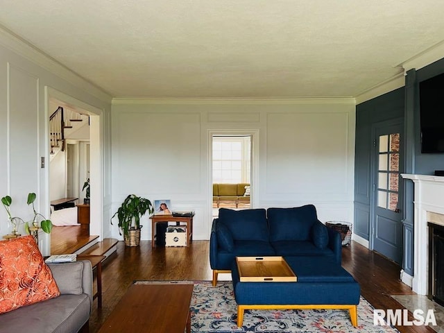 living room with a fireplace with flush hearth, a decorative wall, crown molding, and dark wood-style flooring