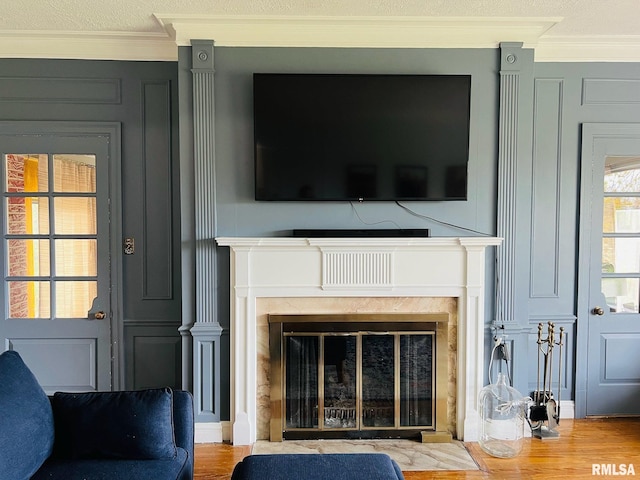 interior details featuring a high end fireplace, a decorative wall, crown molding, and wood finished floors
