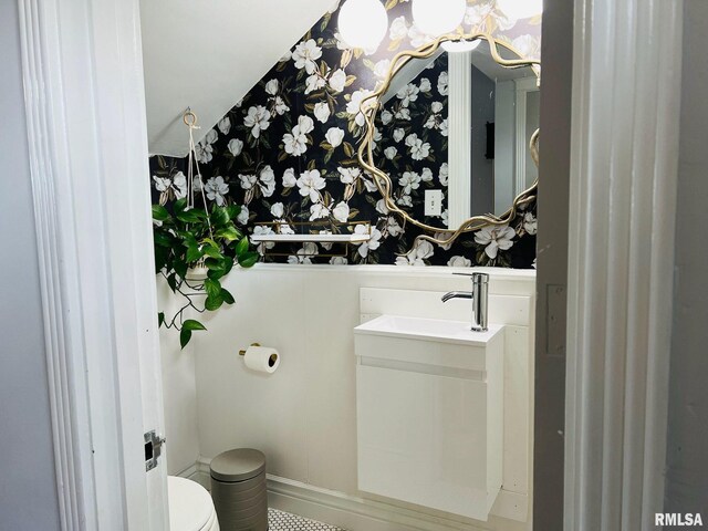 half bathroom featuring wallpapered walls, baseboards, vanity, and toilet