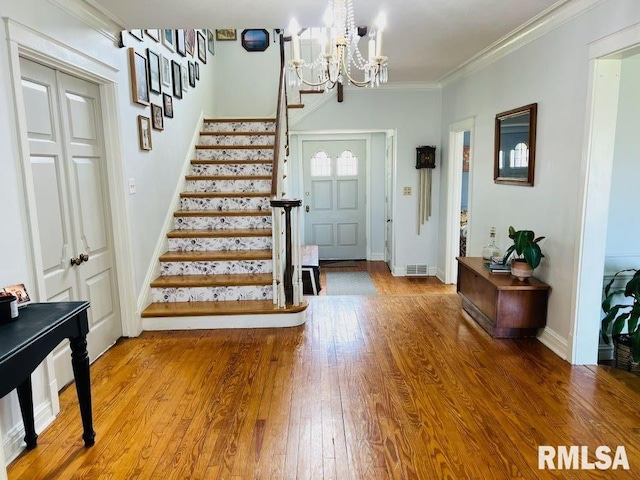entryway with crown molding, stairs, hardwood / wood-style flooring, a chandelier, and visible vents