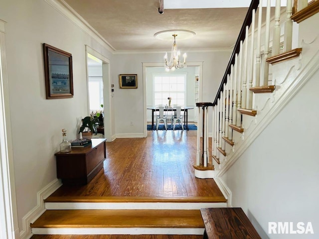 foyer entrance with wood finished floors, ornamental molding, stairway, and an inviting chandelier
