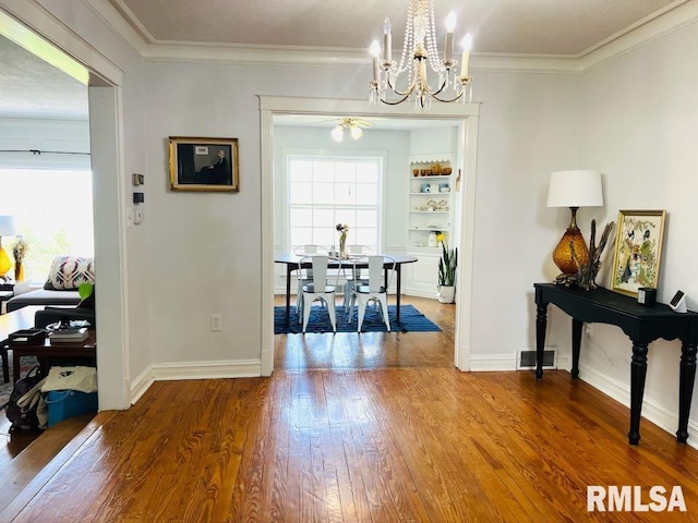 dining room with wood finished floors, a chandelier, baseboards, ornamental molding, and visible vents