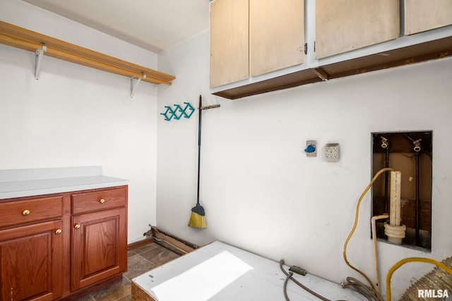 clothes washing area featuring stone finish flooring and cabinet space