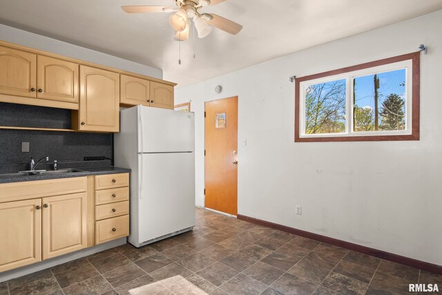 kitchen with dark countertops, a sink, ceiling fan, baseboards, and freestanding refrigerator