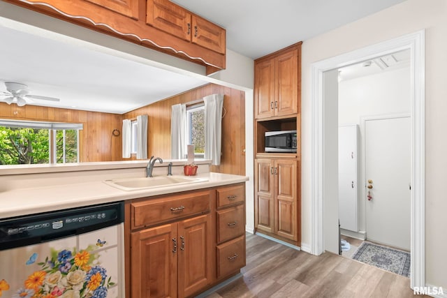 kitchen featuring dishwasher, a sink, light countertops, stainless steel microwave, and light wood-style flooring