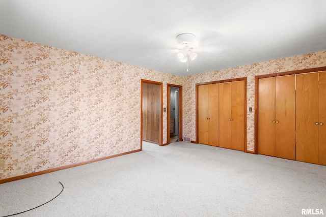 unfurnished bedroom featuring wallpapered walls, multiple closets, and carpet