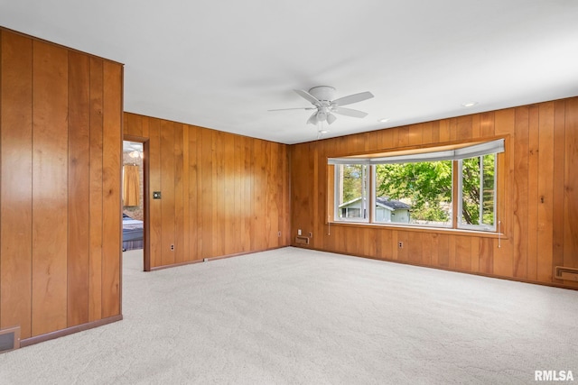 carpeted empty room featuring ceiling fan and wood walls