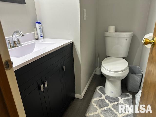 half bath featuring toilet, vanity, wood finished floors, and baseboards