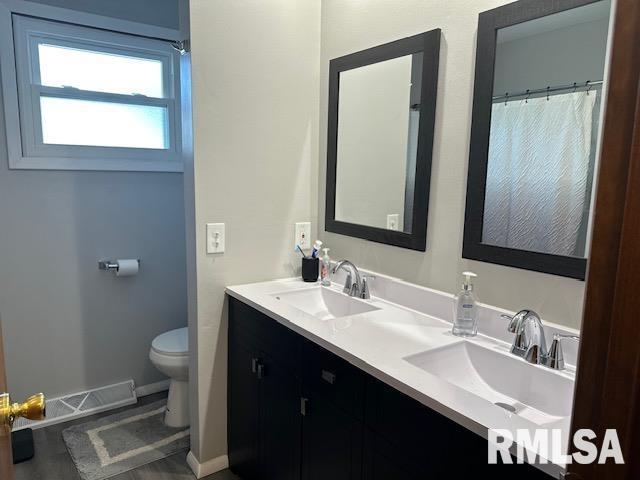 bathroom featuring double vanity, toilet, baseboards, and a sink