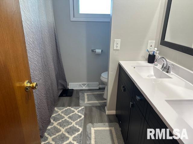 full bathroom with a sink, double vanity, toilet, visible vents, and wood finished floors