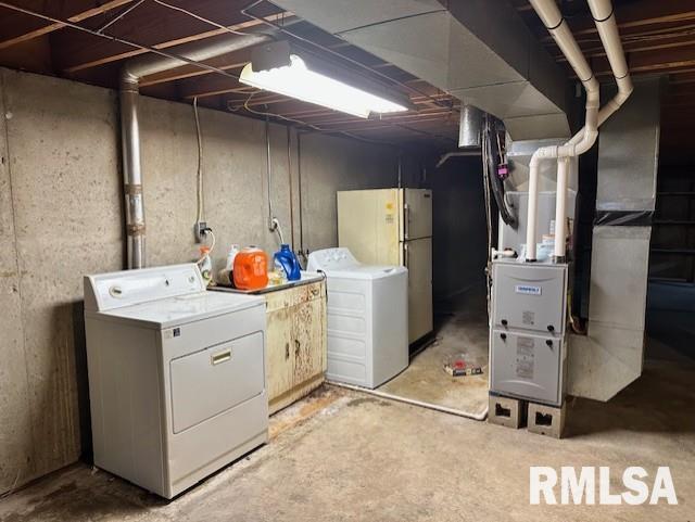unfinished below grade area featuring separate washer and dryer, heating unit, and freestanding refrigerator