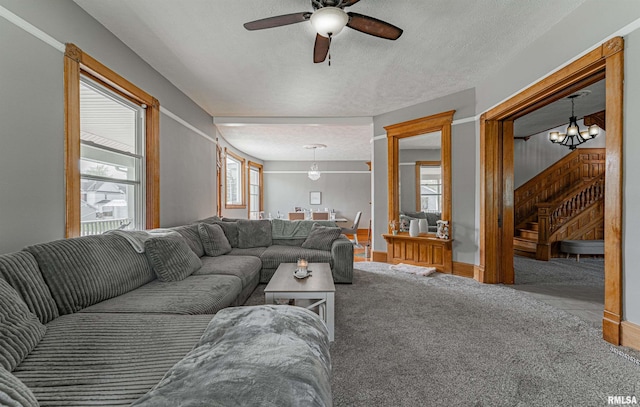 carpeted living room with baseboards, a textured ceiling, stairway, and ceiling fan with notable chandelier