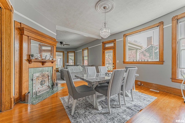 dining area featuring wood-type flooring, a textured ceiling, a tiled fireplace, and baseboards