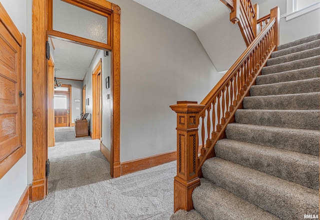 staircase featuring a textured ceiling, carpet flooring, and baseboards