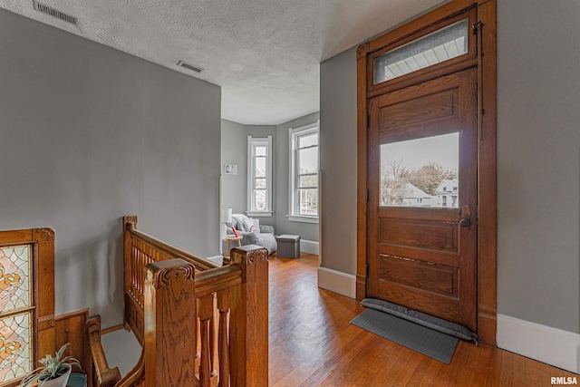 entrance foyer with wood finished floors, visible vents, baseboards, and a textured ceiling